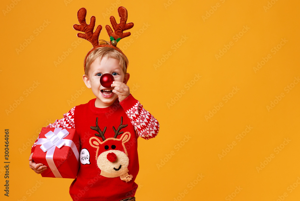 快乐有趣的小男孩，穿着红色圣诞驯鹿服装，黄色背景是礼物