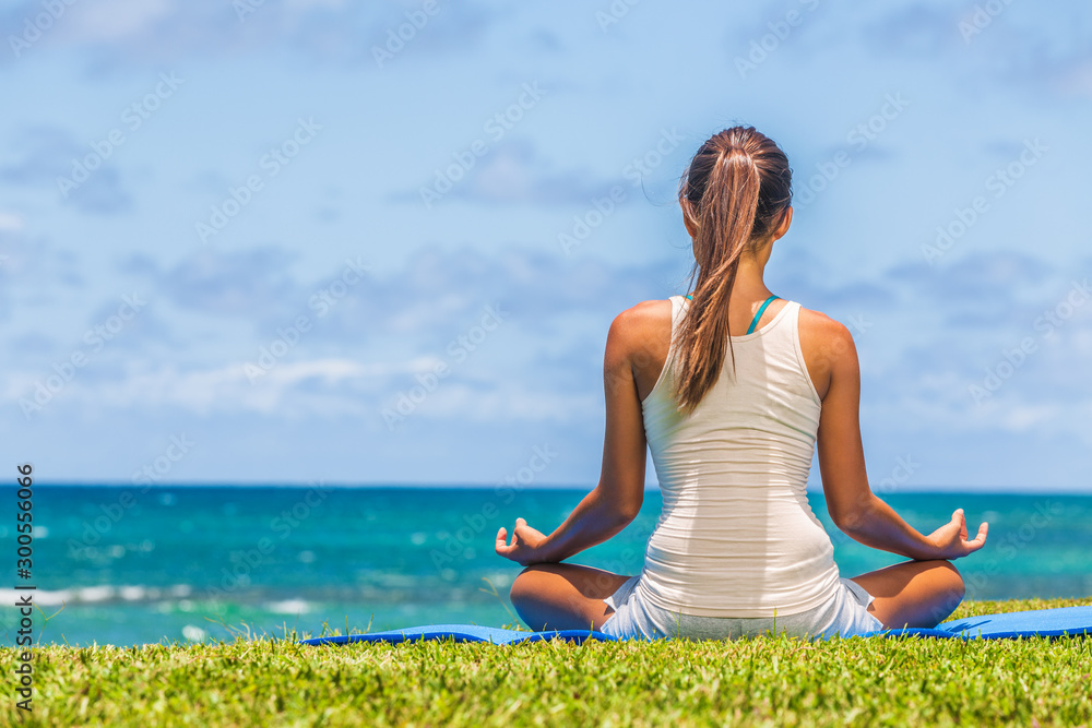 瑜伽冥想女人在沙滩草地上的运动垫上以莲花姿势冥想。