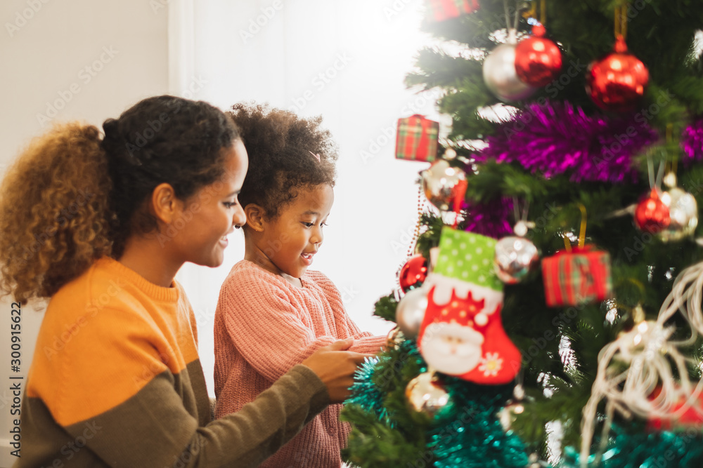 非洲黑人母亲和她可爱的女儿为圣诞节装饰圣诞树，祝你圣诞快乐
