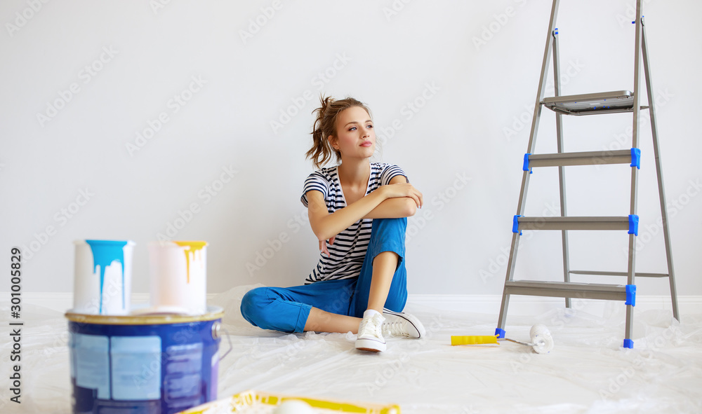 Repair in apartment. Tired young woman paints wall .
