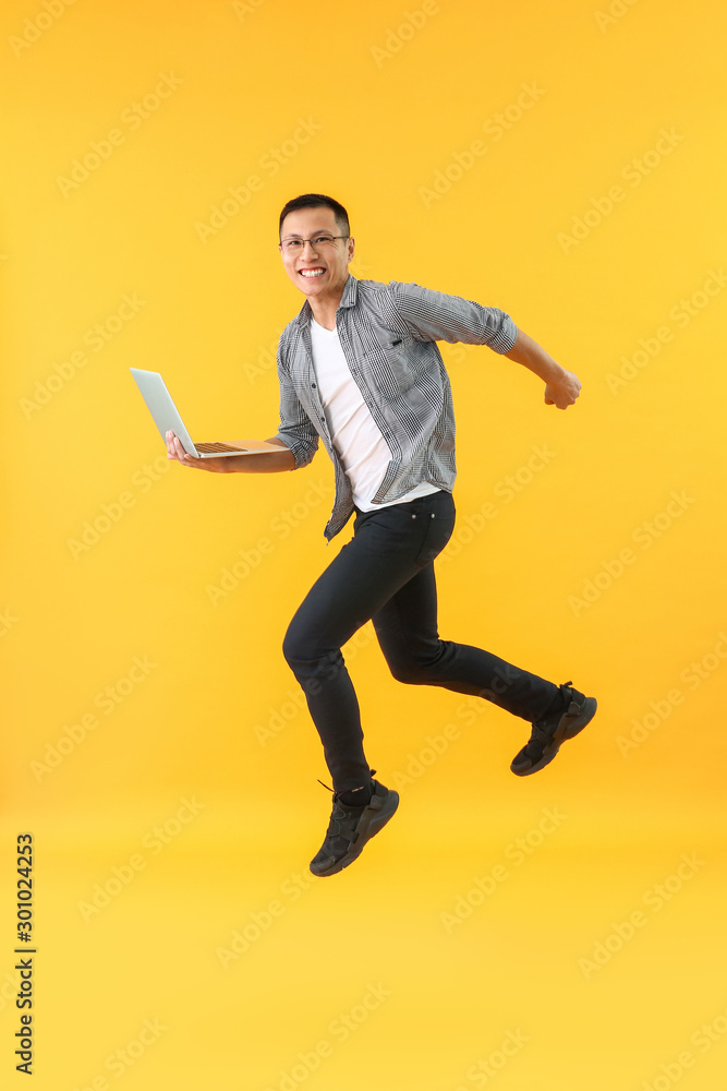 Happy jumping Asian programmer with laptop on color background