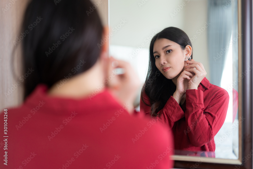 漂亮的亚洲女人穿着红色衣服，戴着星星耳环，在h的卧室里照镜子