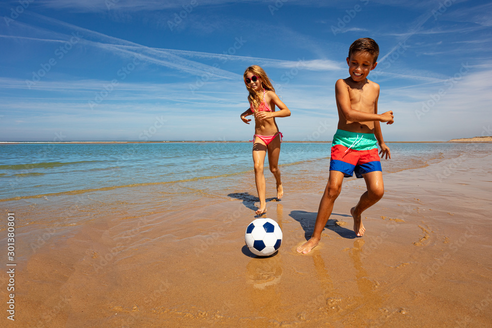 Young boy and girl play soccer ball on the beach