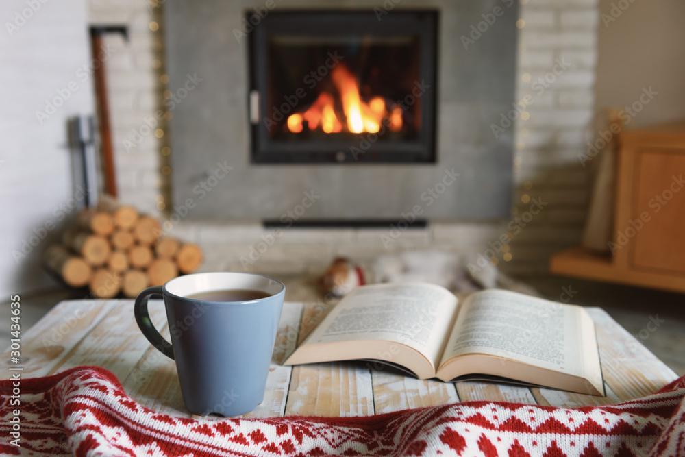 Hygge概念，打开书本，在燃烧的壁炉旁喝杯茶