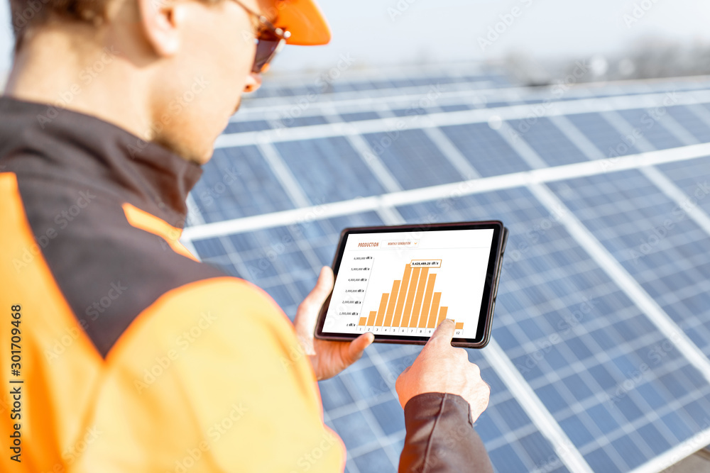 工人正在检查太阳能发电厂的发电情况，手里拿着一块带有电气图表的数字平板电脑