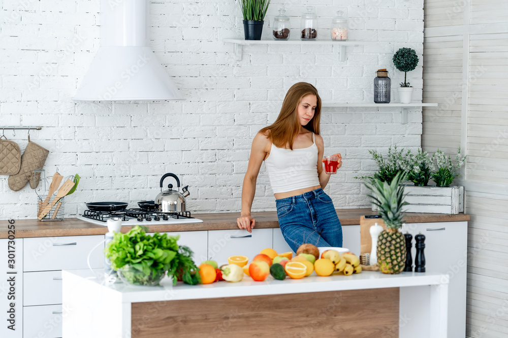 年轻的运动型女性在现代厨房喝健康的红果汁。排毒和节食。水果和蔬菜