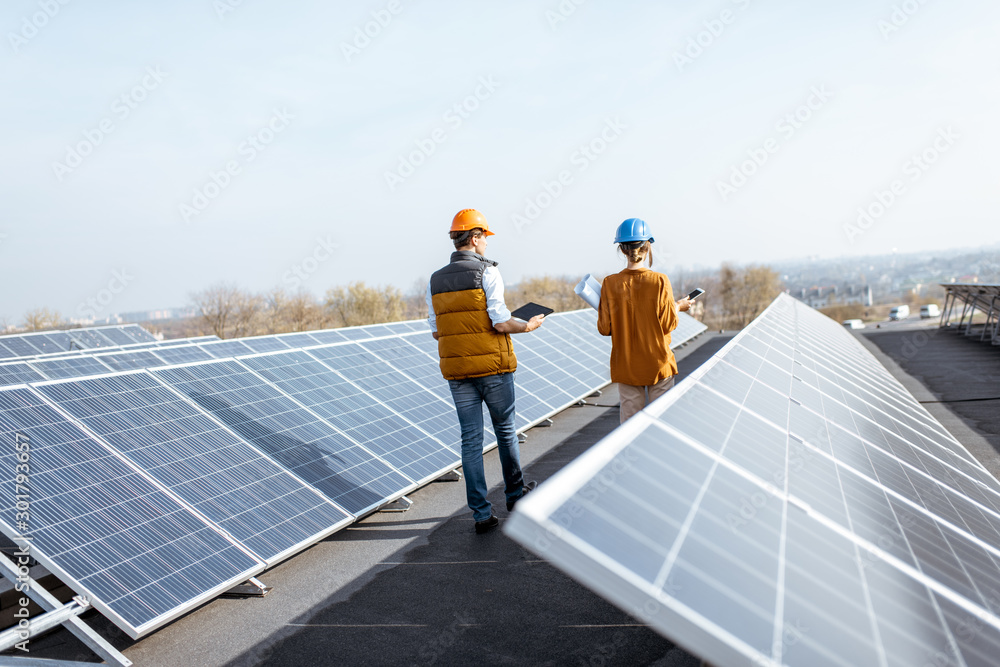 两名工程师在屋顶太阳能发电厂散步，检查光伏电池板。