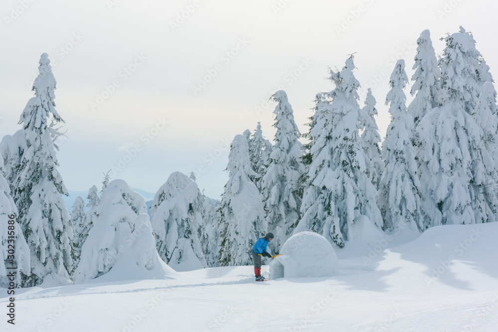 身穿蓝色夹克的男子在高山上建造冰屋。奇妙的冬季场景