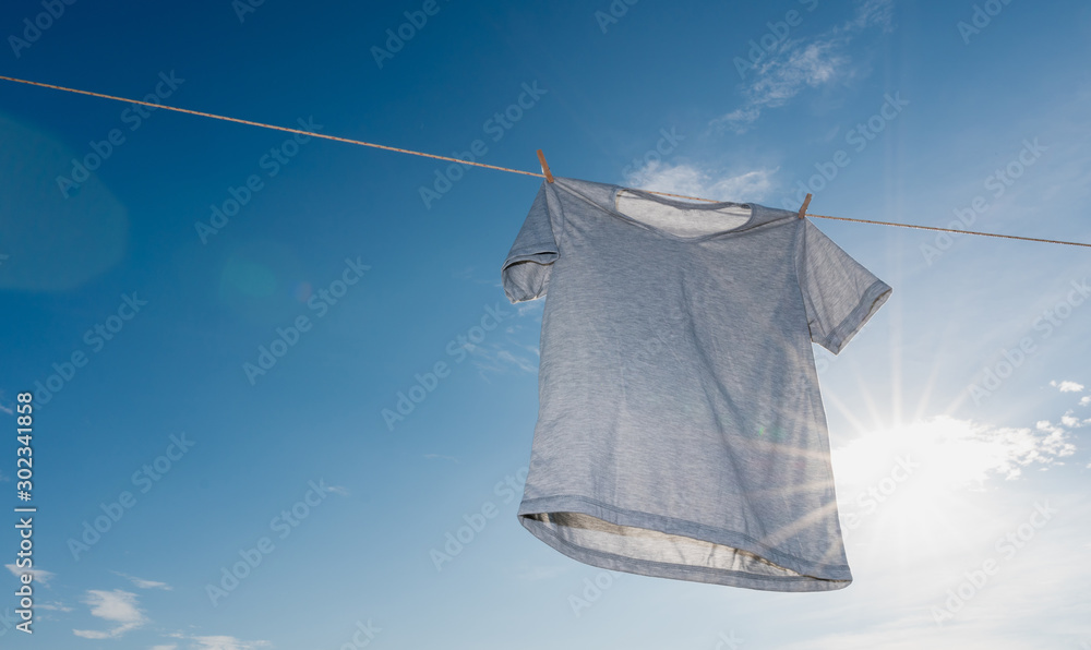 灰色一件干t恤挂在晾衣绳上，阳光照在蓝色的sk里的洗衣概念