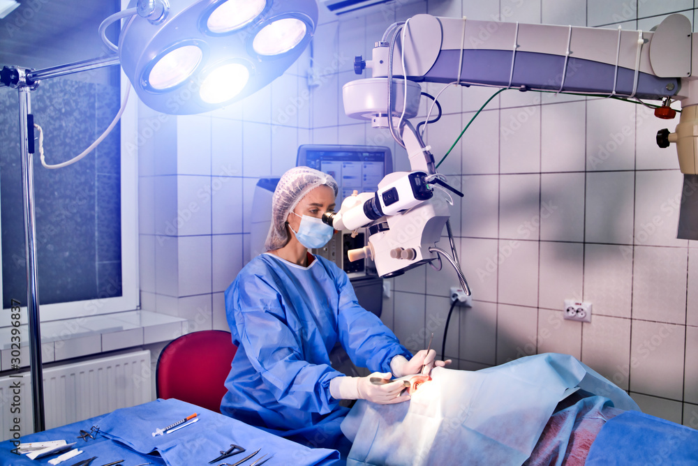 外科医生看着显微镜，手术室的女医生在治疗病人。Selec