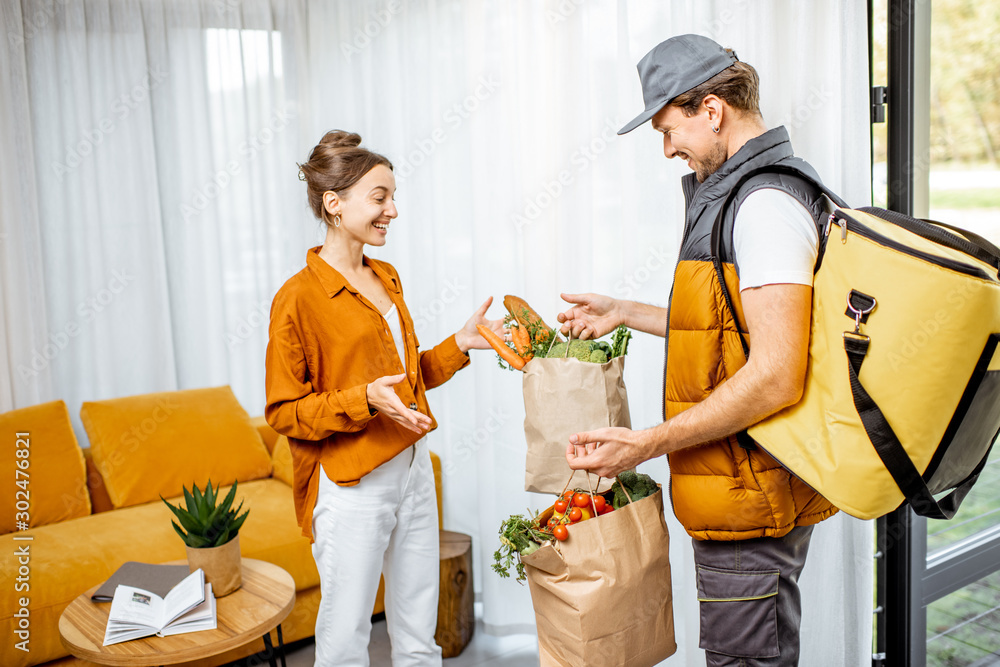 穿着制服、带保温袋的快递员用纸袋将新鲜食品送到一位年轻客户家中。