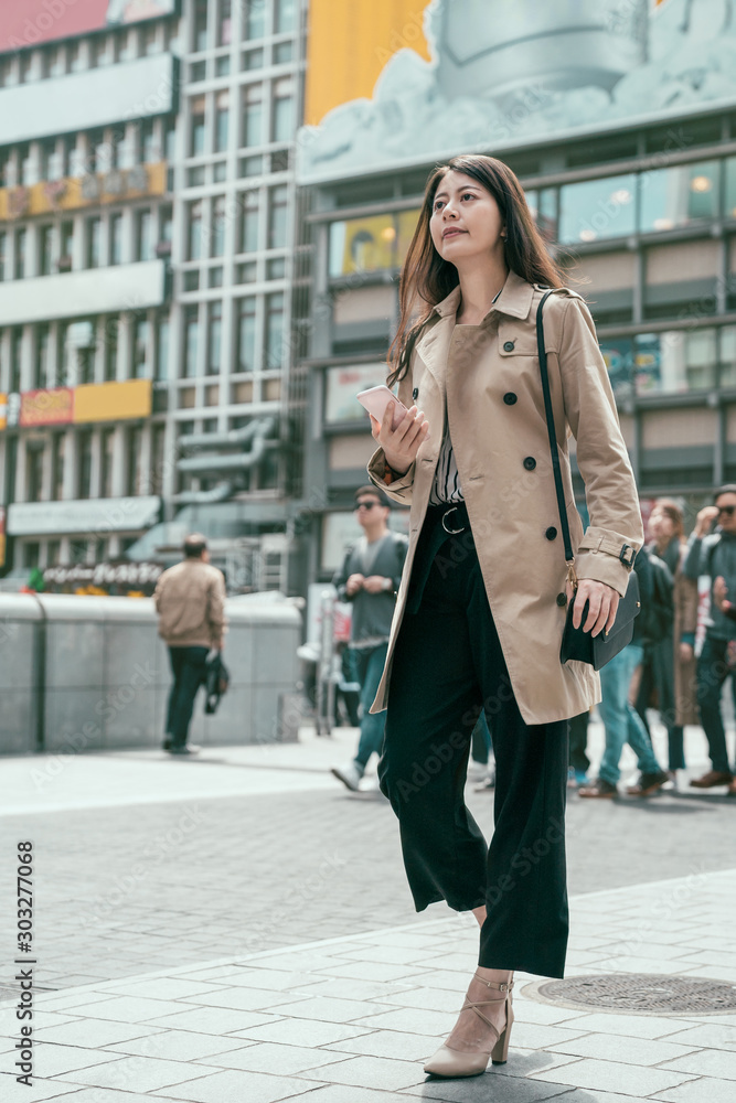 亚洲女性用智能手机在大阪市区行走。下班后漂亮的年轻女士