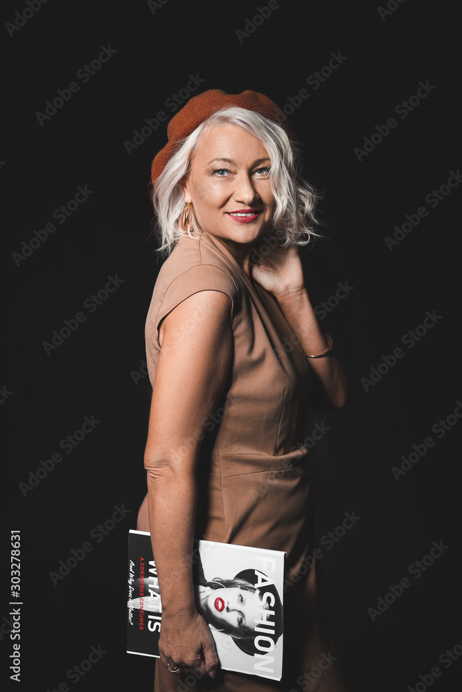Portrait of stylish mature woman with fashion magazine on dark background