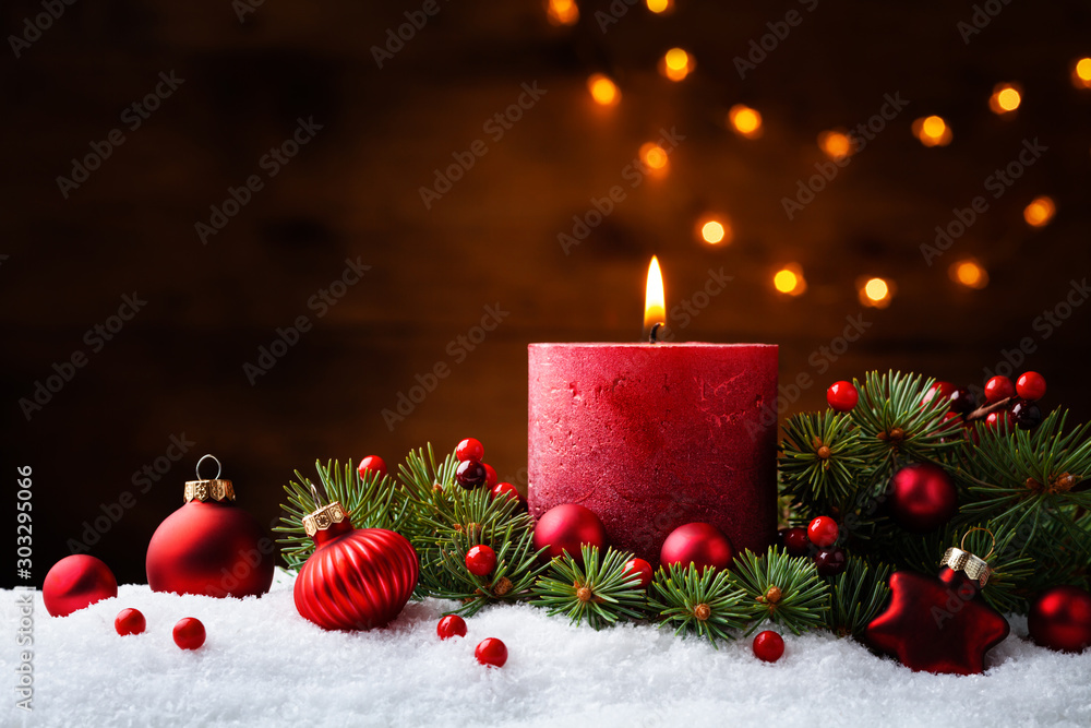 Advent candle, fir tree branches and holiday decorations in snow against light  garland background. 