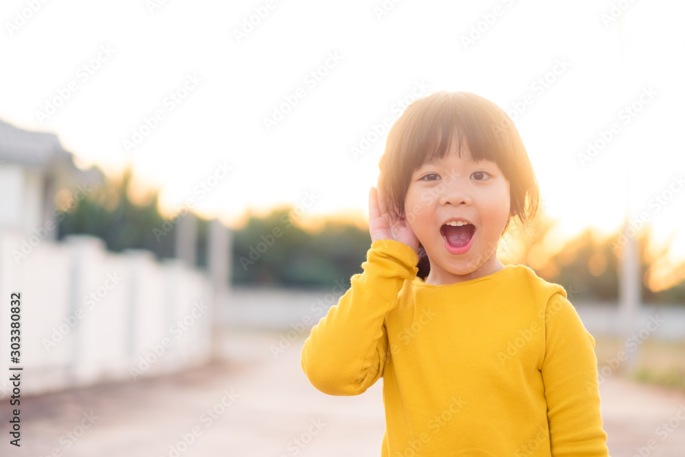 Little asian girl holds her hand near her ear and listening something.Exciting face on funny child g