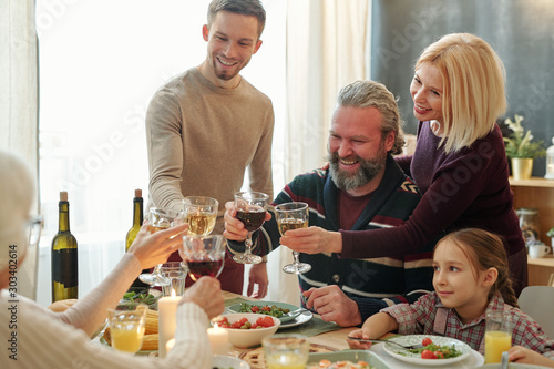 快乐的成熟和年轻的家庭成员在自制食物上用葡萄酒敬酒