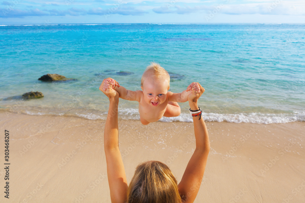 年轻快乐的母亲在白沙海滩上向半空中抛来抛去快乐的男婴。户外健康c