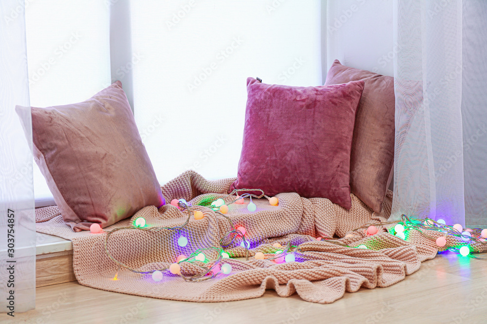 Beautiful glowing garland with pillows and plaid on window sill