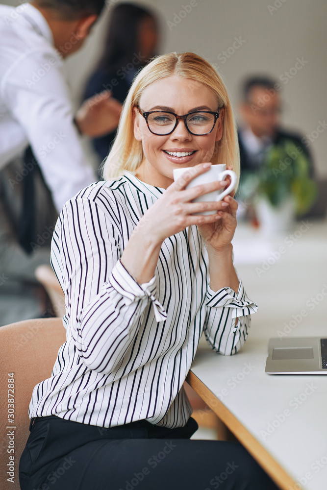 微笑的年轻女商人坐在工作岗位上喝咖啡