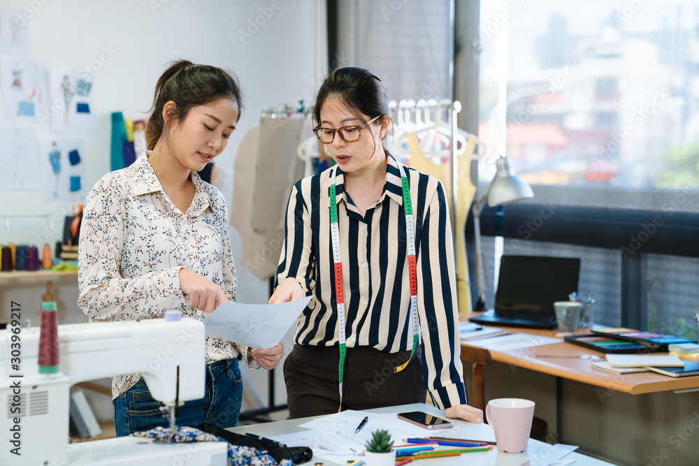 两位亚裔日本女性时装设计师同事创意人员在办公室讨论杂志布局。