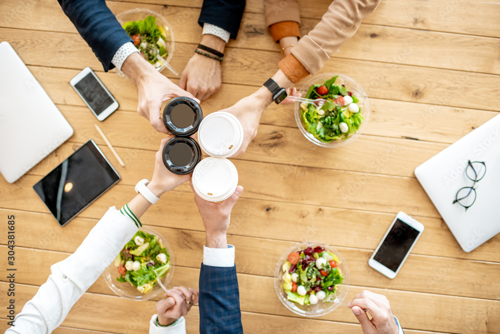 Office workers clinking coffee cups during a business lunch with healthy salads, view from above on 