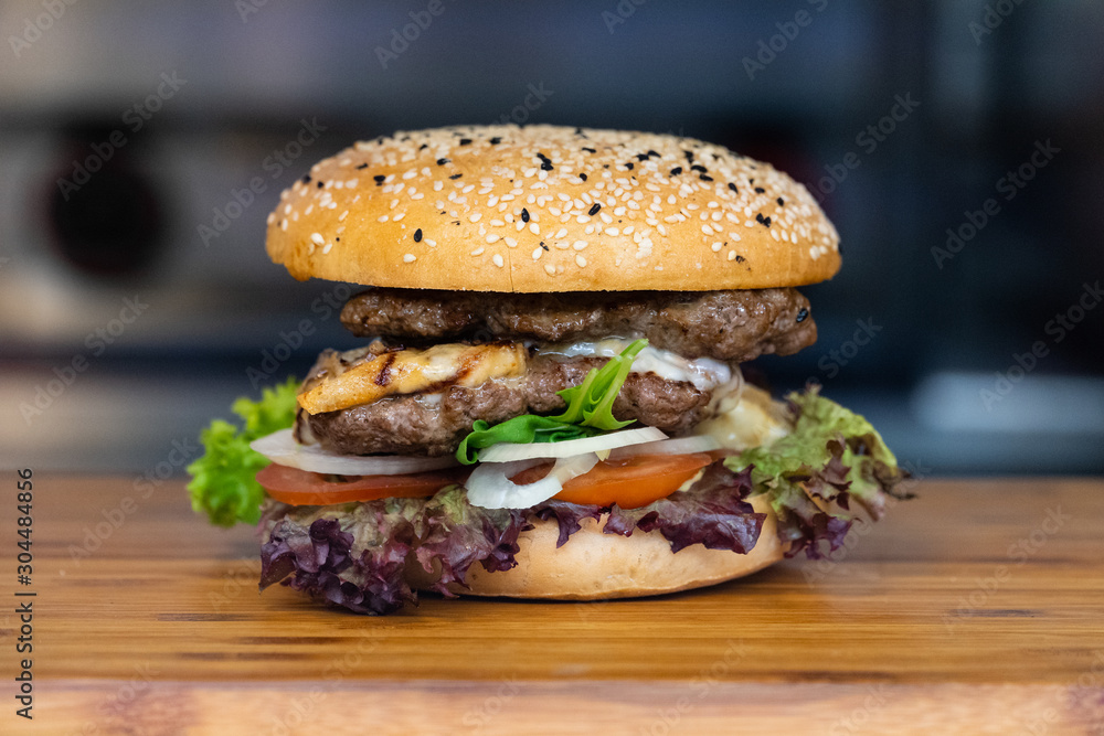 一个大而新鲜的彩色汉堡，里面有肉、蛋、沙拉、洋葱圈和蘸酱，放在木托盘上