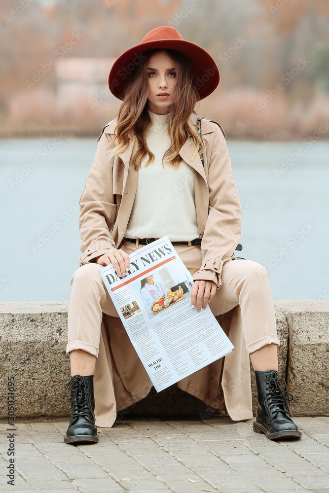 Portrait of stylish young woman with newspaper outdoors