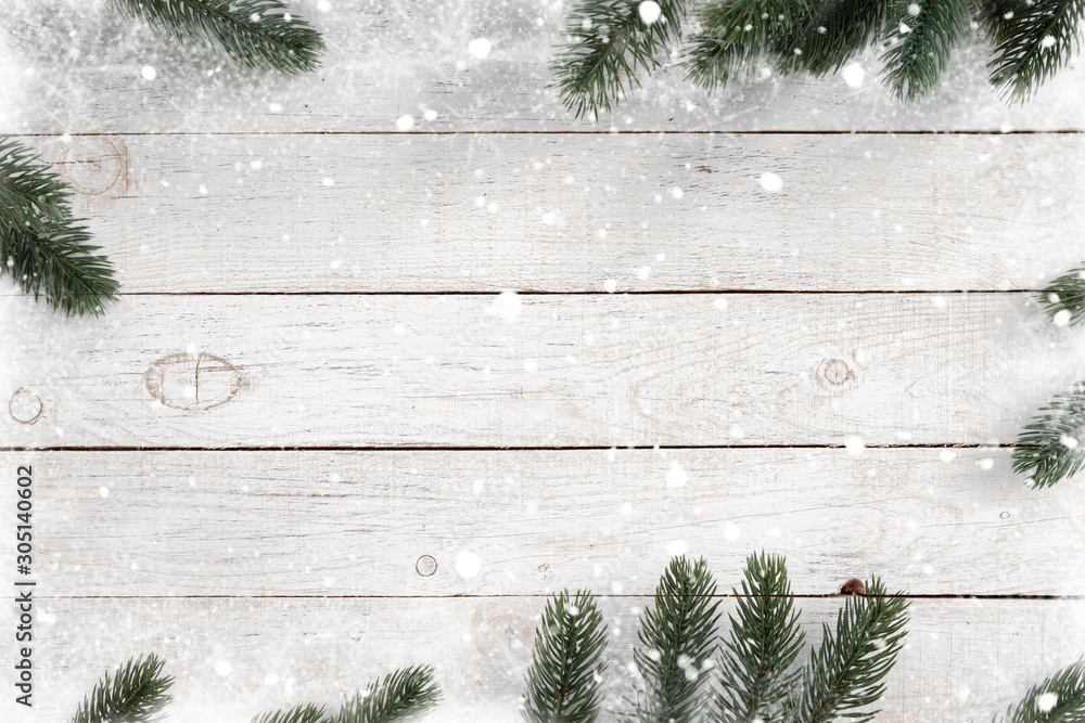 松木叶子装饰成框架，白色木质背景上有雪花。圣诞快乐。