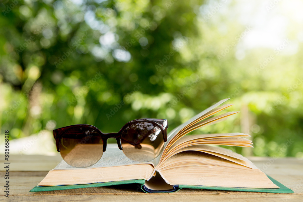 在花园的木桌上打开书本和眼镜。阳光明媚的夏日，在假期里阅读。