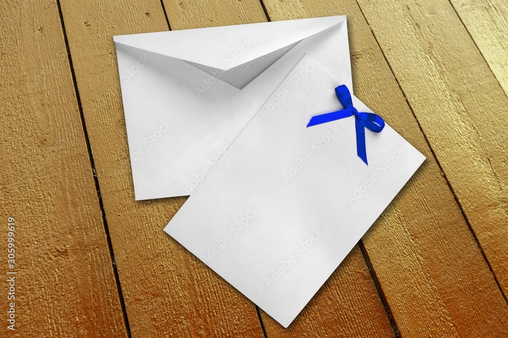 木制背景上带蓝色蝴蝶结和空白字母的邀请信封