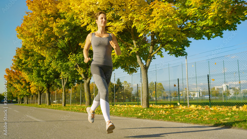 LOW ANGLE: Cinematic shot of a young female jogger running along vibrant walkway