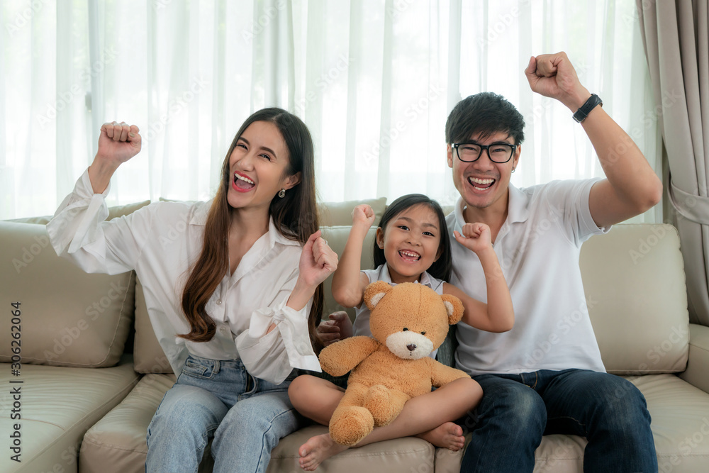 亚洲家庭，父亲、母亲和女儿坐着看电视，看有趣的公关时面带微笑