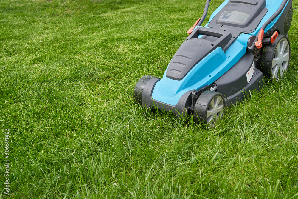 Electric lawn mower mows a bright green overgrown lawn, close-up