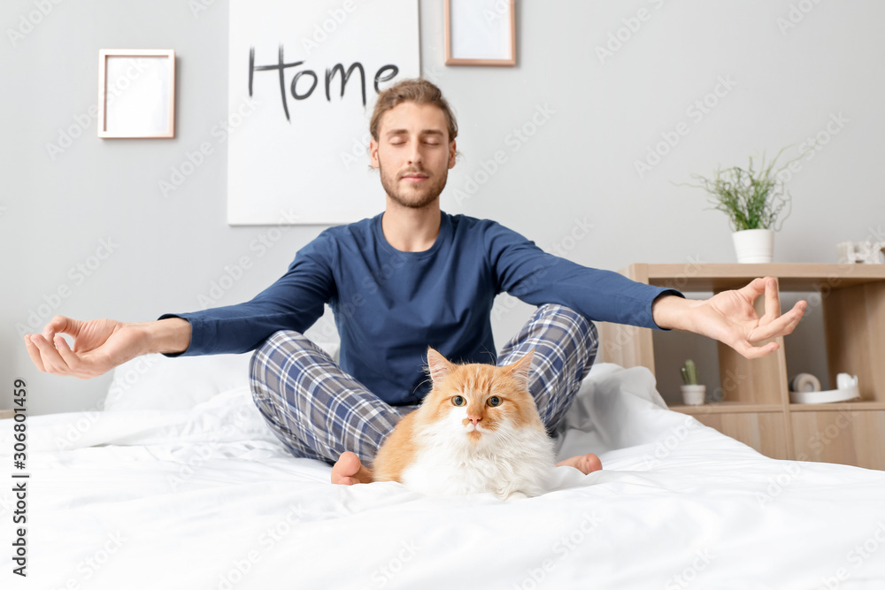 年轻人带着可爱的猫在卧室冥想
