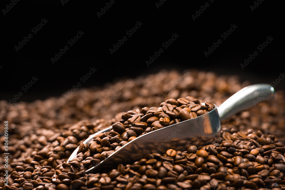 Coffee beans in spoon on pile of coffee beans