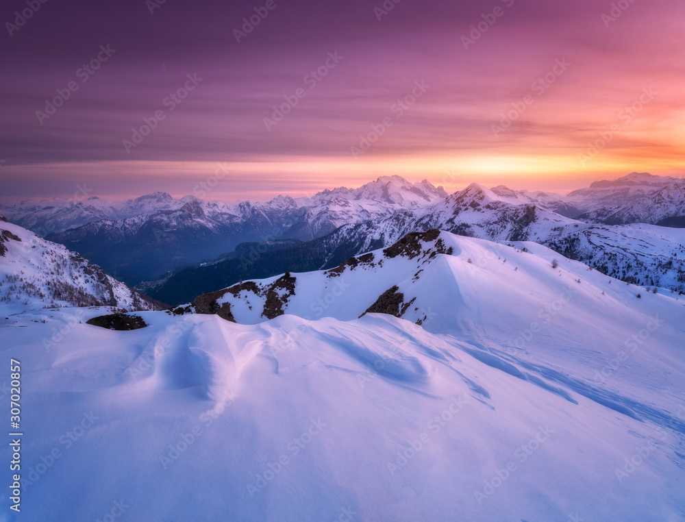 冬天日落时，白雪覆盖的山脉上有五颜六色的红色天空，云朵和明亮的阳光