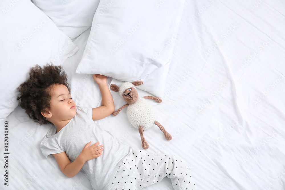 Little African-American girl with toy sleeping in bed