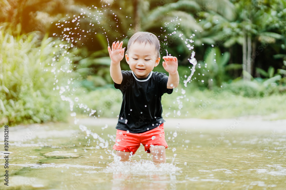 快乐的亚洲蹒跚学步的男孩在大自然的河里玩水玩得很开心。他玩水，做hea