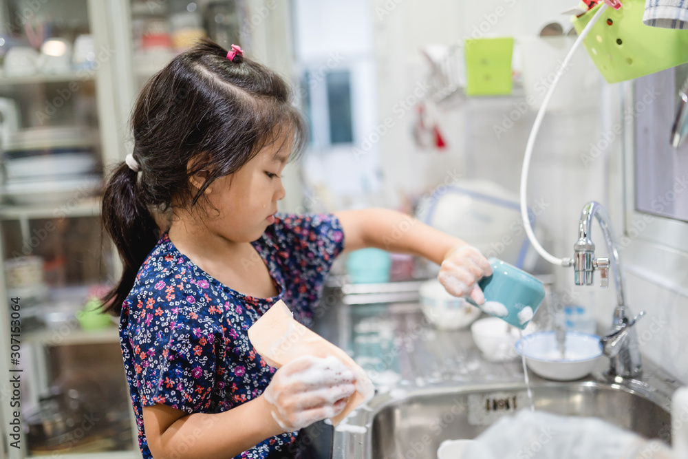 Happy smiley laughing face little cute asian girl washing dishes in kitchen for help her mom.Child d