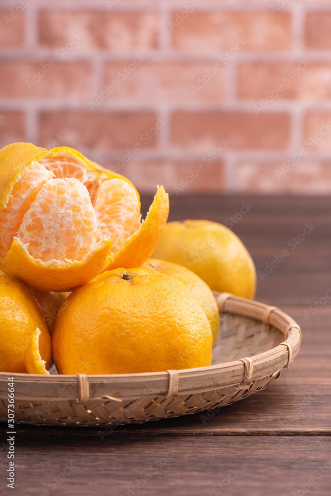Peeled tangerines in a bamboo sieve basket on dark wooden table with red brick wall background, Chin