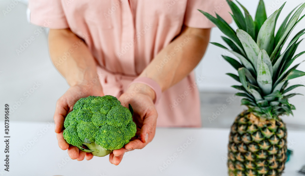 Kitchen and vegetables. Girl holds broccoli in hands. Dieting and health concept. Pineapple on the t