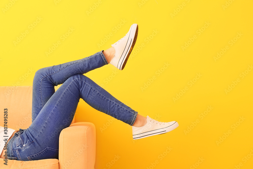 穿着时尚鞋子的年轻女子躺在靠近彩色墙的扶手椅上