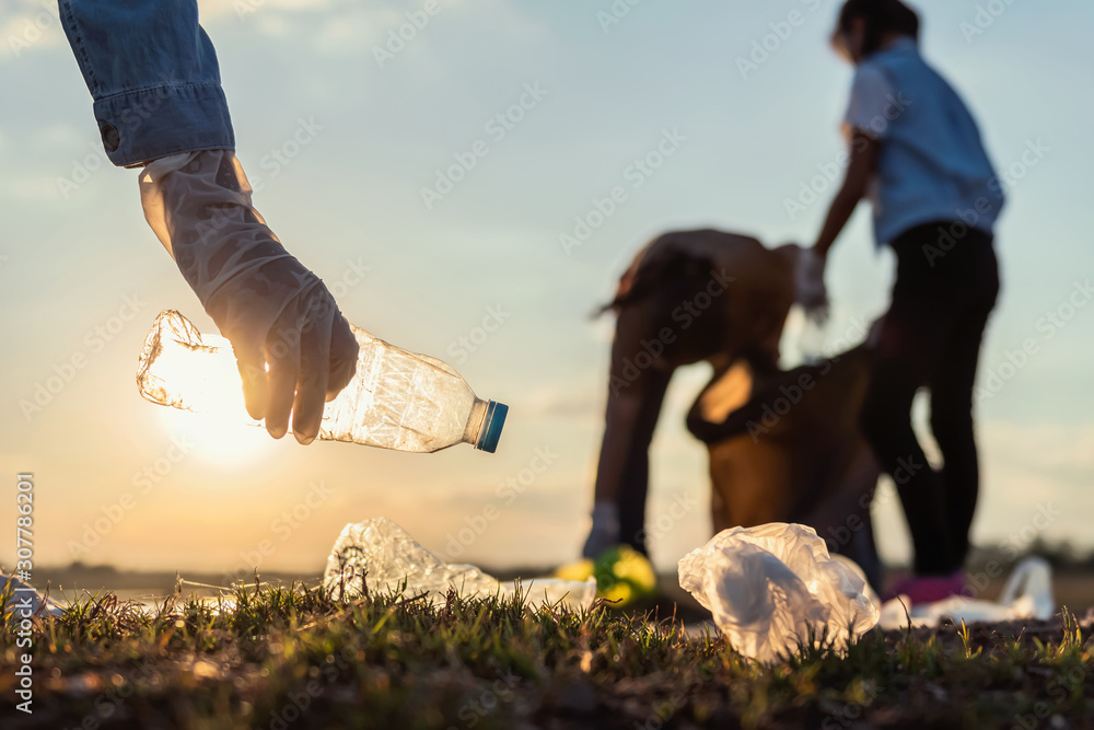 日落时分，人们在公园河边志愿将垃圾塑料瓶放入黑色袋子