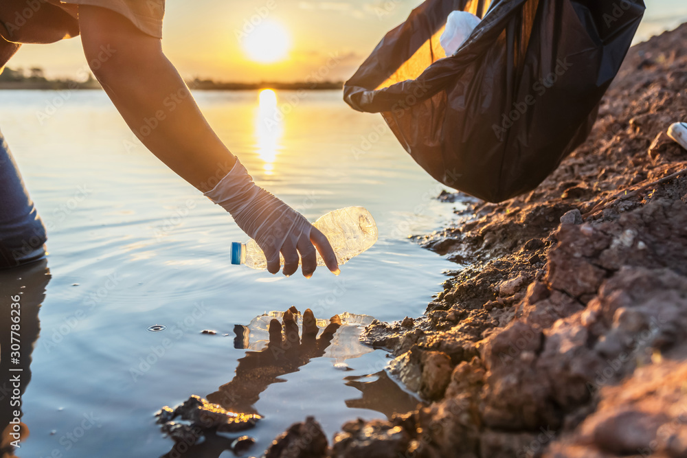 日落时分，人们自愿将垃圾塑料瓶放入河上的黑色袋子中