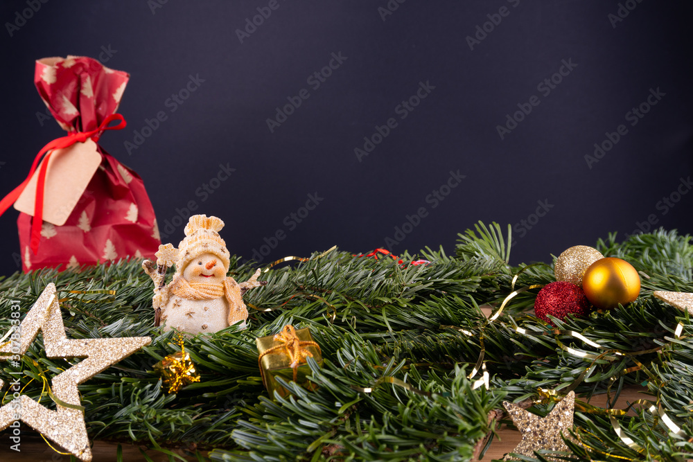 Christmas ornaments (snow man, present, stars, baubles) and fir twigs in front of a black background