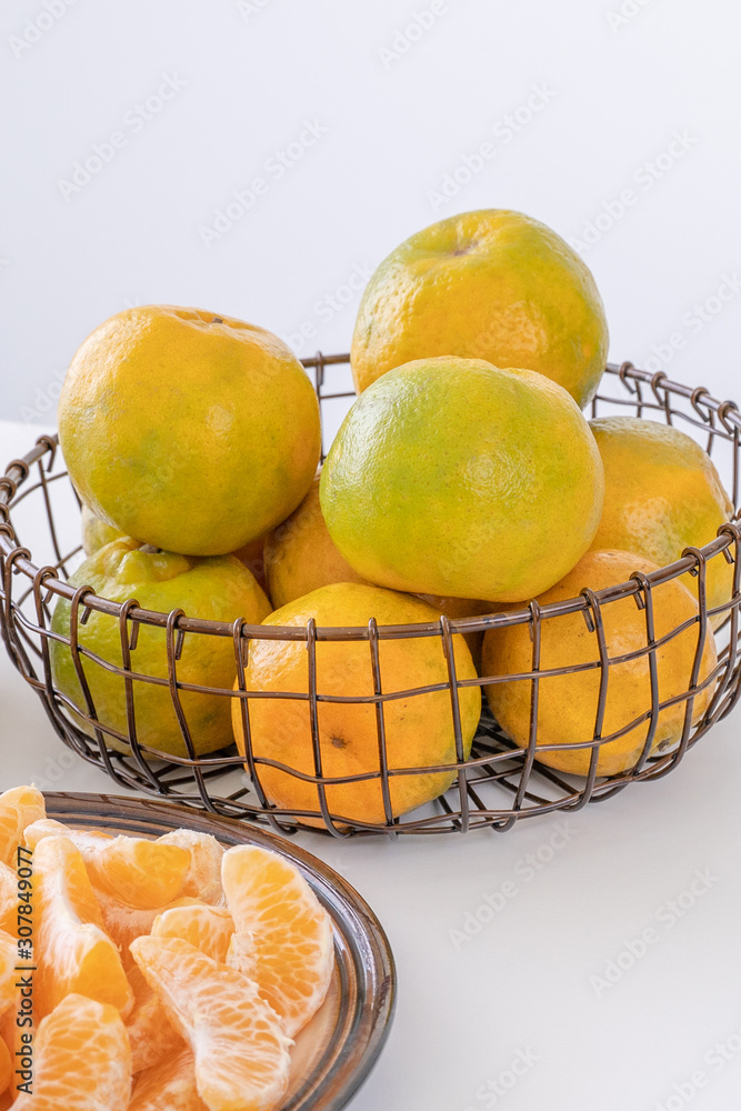 美丽的去皮橘子放在盘子和金属篮子里，在明亮的白色干净的桌子上隔离一个月