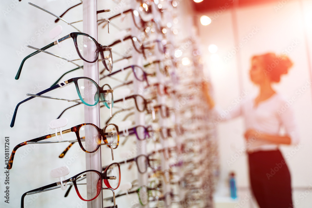 眼镜店。带着眼镜站在眼镜店。背景模糊的女人选择眼镜