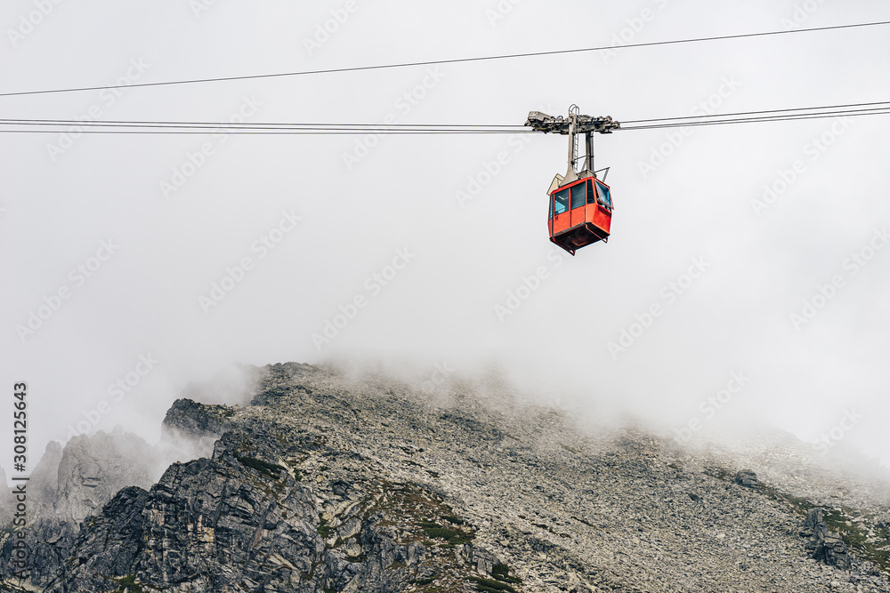 Photo of a cable way in the mountains. Red cableway cabine in the air diving into the clouds. Cablew