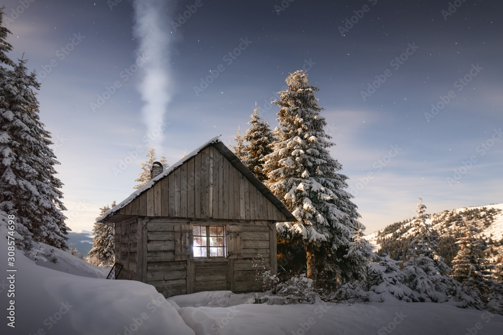 Fantastic winter landscape with wooden house in snowy mountains. Smoke comes from the chimney of sno