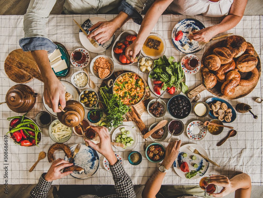 人们坐在桌子旁，享用土耳其早餐，包括糕点、蔬菜、蔬菜和奶酪